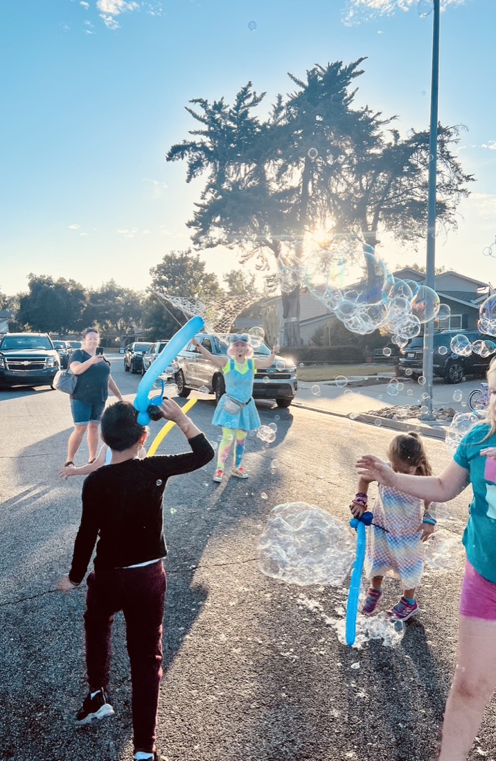 Children chasing bubbles with Miss Molly at a neighborhood block party