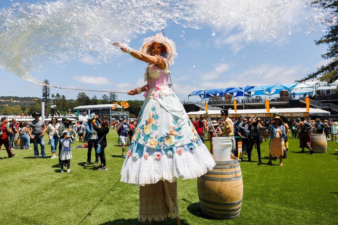 Miss Molly performing on stilts beneath a cloud of bubbles at an outdoor festival