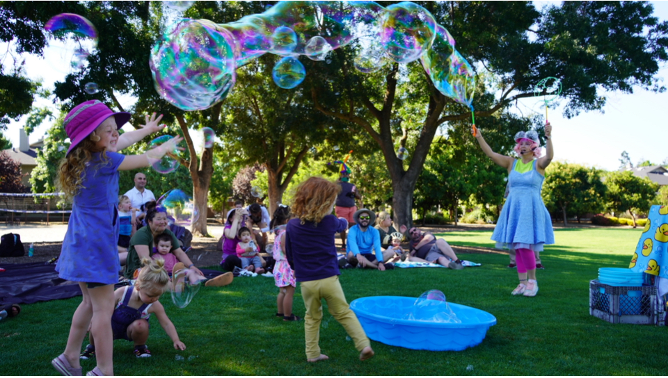Miss Molly making giant bubbles with children in the park