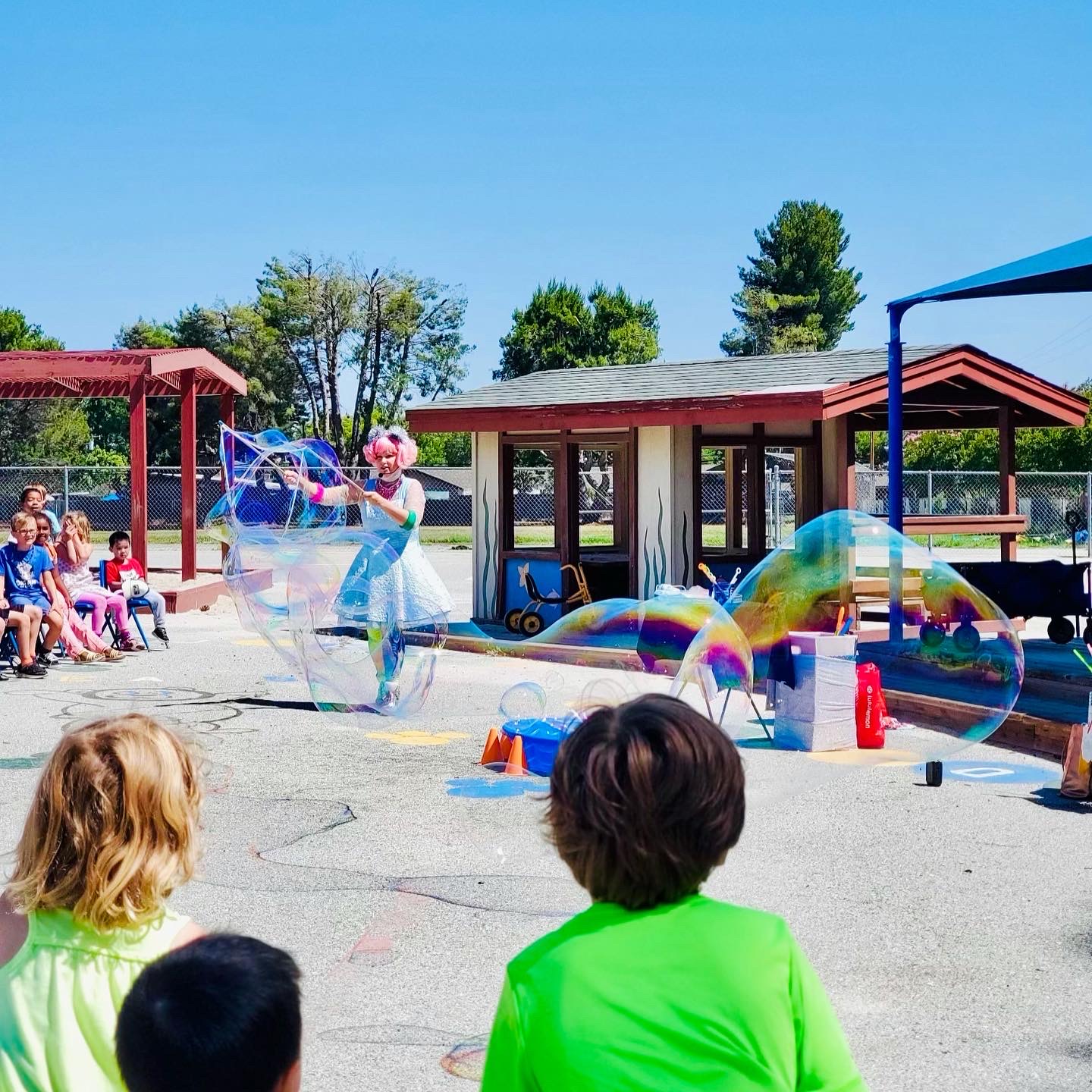 Miss Molly making giant bubbles for children seated outside
