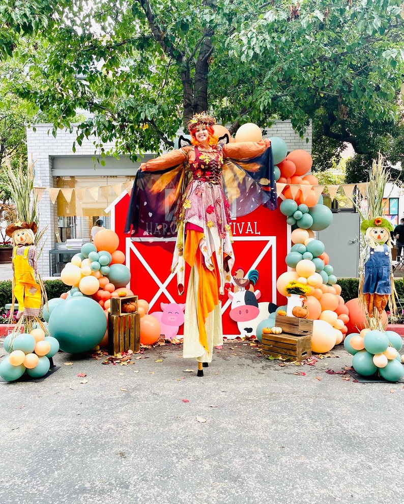 Miss Molly on stilts in an autumn fairy costume with orange leaves and butterfly wings