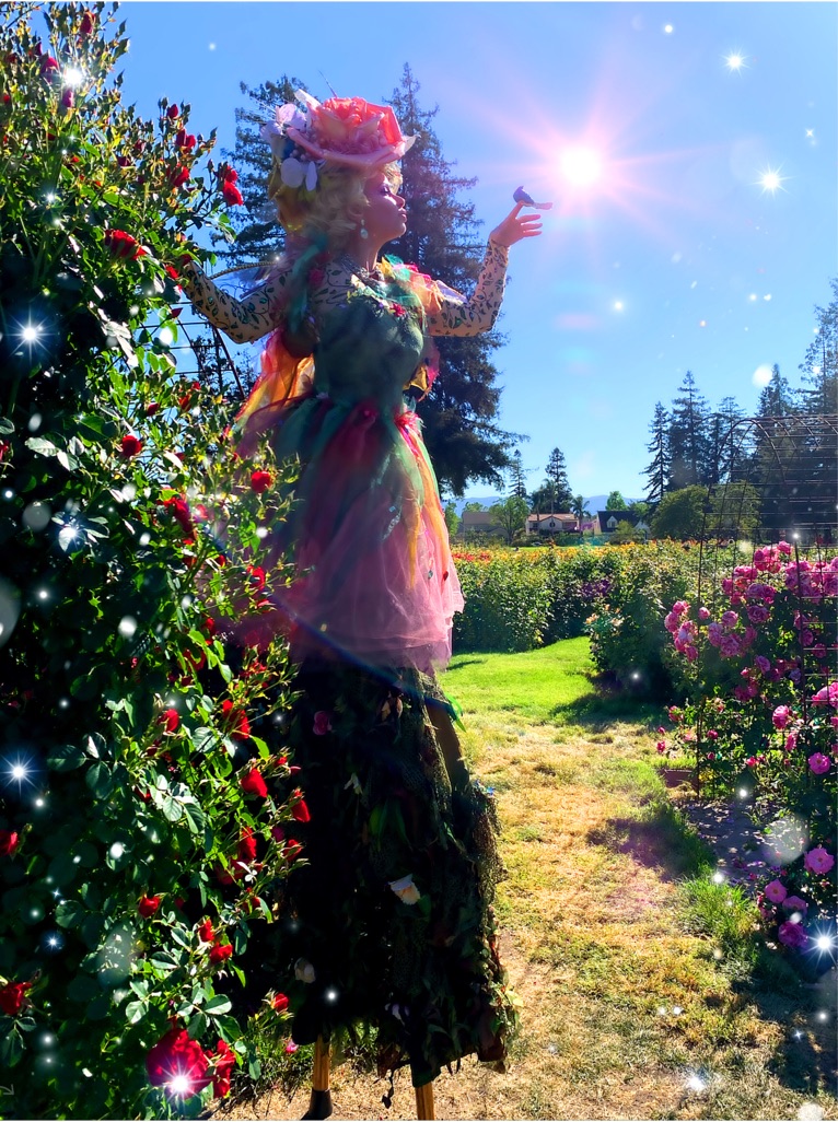 Miss Molly in a flower fairy costume on stilts in a sunny garden