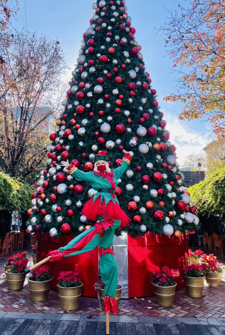 Miss Molly on stilts in a holiday elf costume