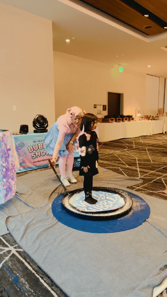 Miss Molly lifting a giant bubble around a guest at an indoor bubble party