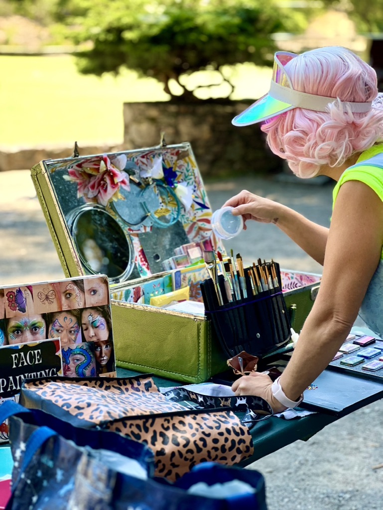 Miss Molly at her face-painting station with paints, brushes and design examples