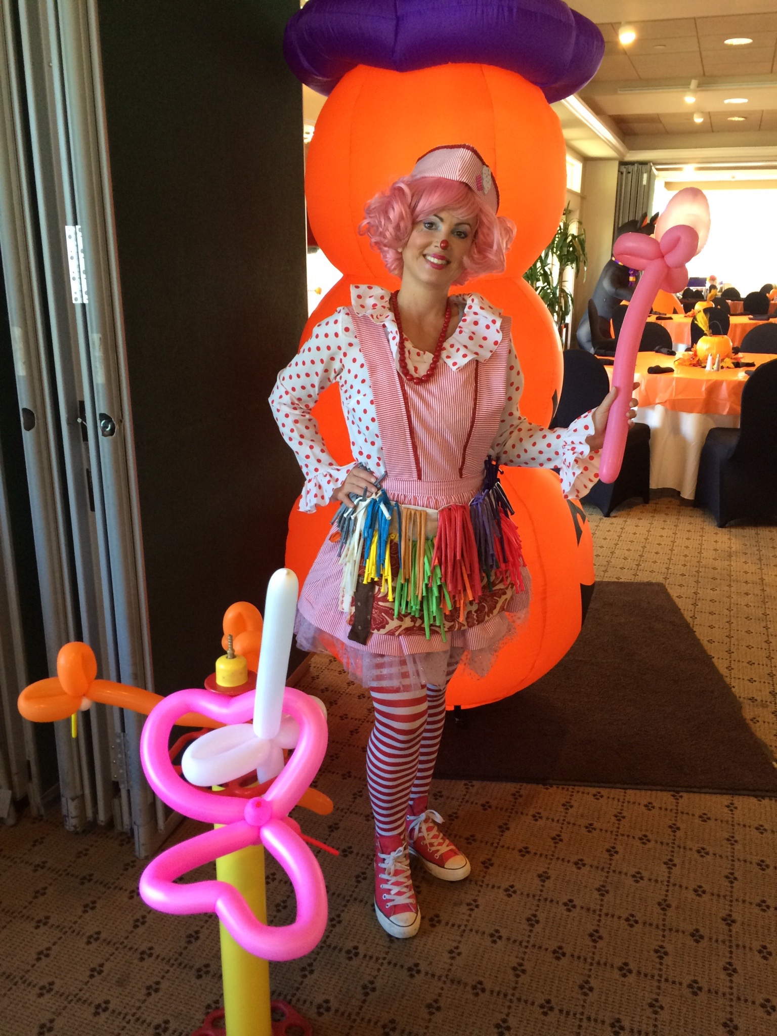 Miss Molly holding twisted balloons at an indoor event